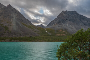 Beautiful landscape with rocky mountains and turquoise sea. A river streaming between mountains. Cloudy sky.