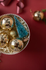 Christmas decorations in the round gift box with fir tree on the red background. Close up winter holidays greeting card.