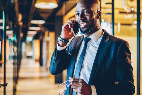 Cheerful black businessman speaking on smartphone in office hallway