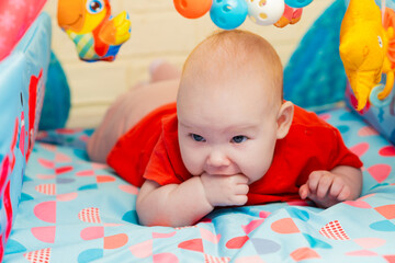 A close-up portrait of a cute adorable newborn baby with blue eyes licking his sucking fingers with a fist. The child is teething.