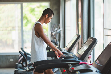 Asian athlete tan skin sport man runner touch start buttom before workout running on treadmill in...