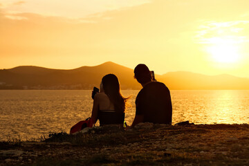 Silhouette of girl admiring beautiful sunset sitting on stone on sea coast. Silhouette of a man and...