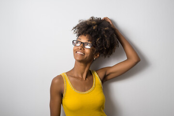 Young black casual woman wearing glasses and looking up. Afro hairstyle cheerful model against white wall.