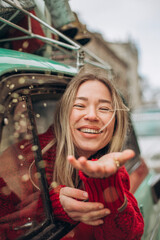 Young blonde woman peeking through a car window and blowing on a shining glitter confetti