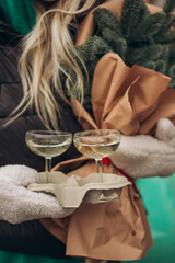 A blonde girl in mittens holds two glasses of champagne in cup holders and a Christmas bouquet