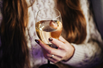 Woman drinking wine. White wine drinking. Wine glass in hand. Girl in woolen sweater. Cozy winter alcohol background. Female hand holding wine glass. Winter season clothing. Shallow depth of field.
