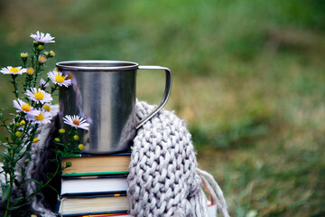 A cup of coffee on a background of books and a blanket. Composition of a mug of coffee, flowers, books and a blanket in nature.