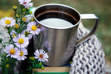 Obraz na płótnie Canvas A cup of coffee on a background of books and a blanket. Composition of a mug of coffee, flowers, books and a blanket in nature.