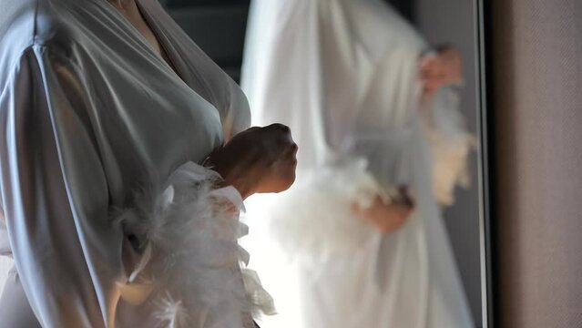 beautiful elegant woman in silk dressing gown is standing in mirror and dressing herself up