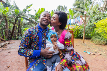 Wife gives husband a kiss on the cheek, husband holds newborn son, united and happy African family