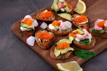 Assorted bruschetta with seafood, shrimp and caviar, avocado, cheese and radish on wooden board