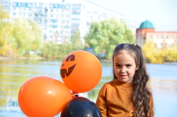Fototapeta na wymiar happy laughing child girl in witch costume to halloween. with a jack-o'-lantern candy bowl, trick or treat, in a witch's hat, with colorful balls in the autumn forest, eating spider-shaped candy