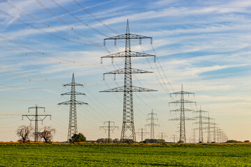 Strommasten und Freileitungen bis zum Horizont in ländlicher Umgebung bei Sonnenuntergang