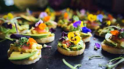 Canapes with avocado, cream cheese and edible flowers on a black background