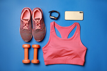 Naklejka premium Stylish sportswear, dumbbells and smartphone on blue background, flat lay