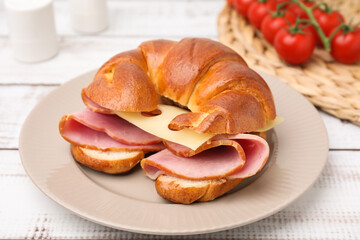 Tasty crescent roll with ham and cheese on white wooden table, closeup