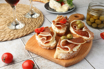 Tasty sandwiches with cured ham, tomatoes and olives on tiled table