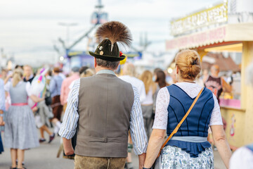 Man wearing Lederhosen and woman wearing the traditional Bavarian Dirndl at the Oktoberfest in Munich, Germany walking side by side close-up - obrazy, fototapety, plakaty