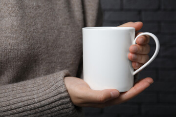 Woman holding white mug on gray background, closeup. Mockup for design