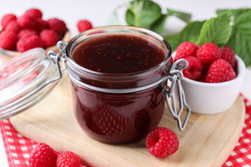 Jar of delicious raspberry jam and fresh berries on table, closeup
