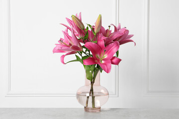 Beautiful pink lily flowers in vase on light grey table against white wall