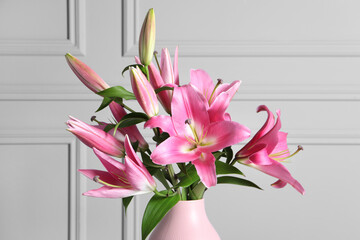 Beautiful pink lily flowers in vase against light wall