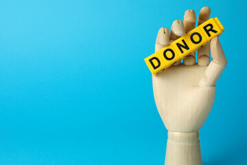 Mannequin hand holding word Donor made of cubes on light blue background. Space for text