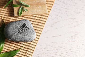 Stone with acupuncture needles and leaves on white wooden table, top view. Space for text