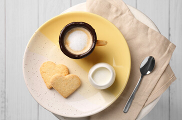 Delicious edible biscuit cup with coffee, milk and heart shaped cookies on white table, flat lay