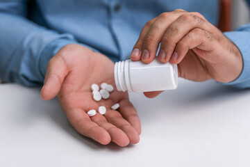 Man pouring antidepressants from bottle at white table, closeup - obrazy, fototapety, plakaty