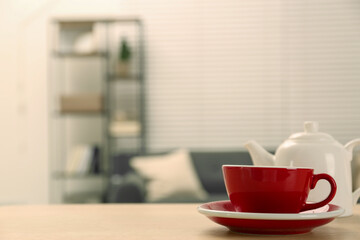 Red cup and saucer on wooden table in room, space for text