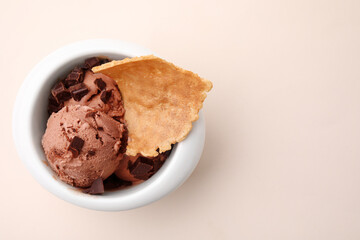 Tasty chocolate ice cream and piece of waffle cone in bowl on beige background, top view. Space for text