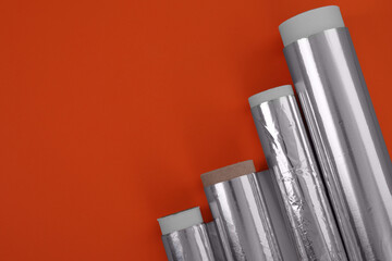 Rolls of aluminum foil on red background, flat lay. Space for text