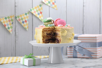 Delicious cake decorated with macarons and marshmallows and gift boxes on white marble table