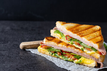 Panini sandwich with ham, cheese, tomato and arugula on black slate background. Copy space