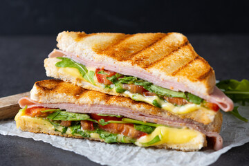 Panini sandwich with ham, cheese, tomato and arugula on black slate background