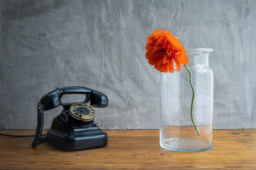 Retro old black rotary telephone on table and poppy