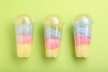 Colorful cotton candies in plastic cups on light green background, flat lay