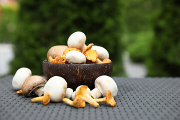 Bowl with different fresh mushrooms on grey rattan table outdoors. Space for text
