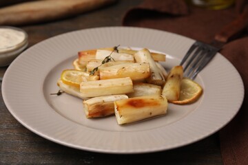 Plate with baked salsify roots, lemon, thyme and fork on wooden table, closeup