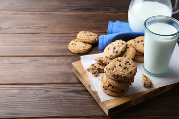 Delicious chocolate chip cookies and glass of milk on wooden table, space for text