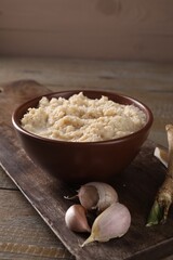 Spicy horseradish sauce in bowl and garlic on wooden table