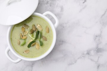 Delicious broccoli cream soup with pumpkin seeds on white marble table, top view. Space for text