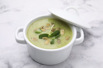 Delicious broccoli cream soup with pumpkin seeds on white marble table, closeup