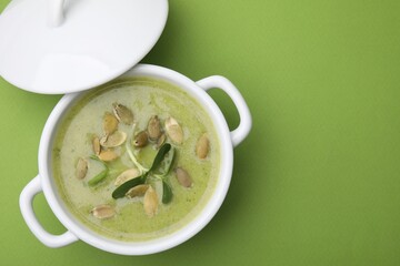 Delicious broccoli cream soup with pumpkin seeds on green background, top view. Space for text
