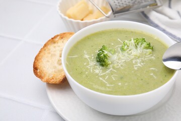 Delicious broccoli cream soup with cheese served on white tiled table, closeup. Space for text