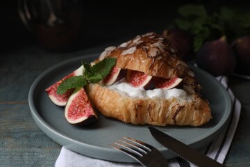 Delicious croissant with figs and cream served on light blue wooden table, closeup