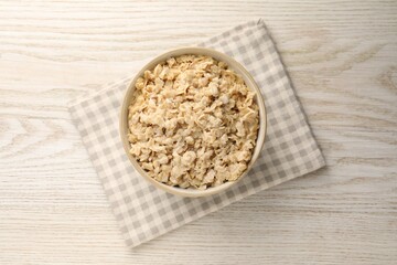 Tasty boiled oatmeal in bowl on light wooden table, top view