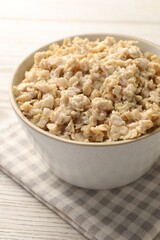 Tasty boiled oatmeal in bowl on light wooden table, closeup