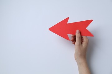 Woman holding red paper arrow on white background, top view. Space for text